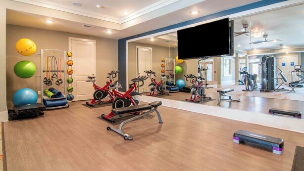 A gym with exercise equipment, a large mirror, and a ceiling fan. - Landing | Incredible 2BD, Gym (Gainesville)