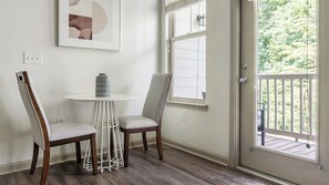 A room with a white door leading to a balcony, two chairs, a small round table, and a wall-mounted abstract artwork. - Landing | Beautiful 1BD, Gym (Gainesville)