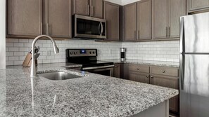 A kitchen with granite countertops, stainless steel appliances, and wooden cabinets. - Landing | Beautiful 1BD, Gym (Gainesville)