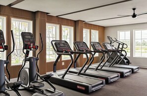 A gym with treadmills and elliptical machines, large windows, and a ceiling fan. - Landing | Modern 1BD, Pool, Gym (Port Charlotte)