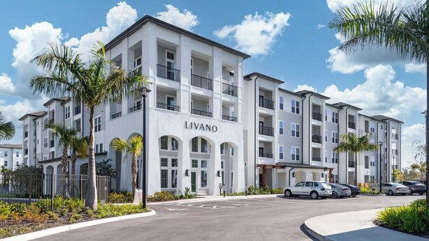 A multi-story building with a white facade, balconies, and a parking area with cars. - Landing | Modern 1BD, Pool, Gym (Port Charlotte)