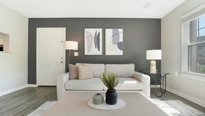 A modern living room with a gray accent wall, a white door, a sofa, two floor lamps, and a potted plant. - Landing | Modern 1BD, Pool, Gym (Port Charlotte)