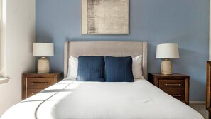 Ein Hotelzimmer mit einem großen Bett, zwei Nachttischen, einem Kopfteil und einem Wandbild.