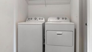 Zwei übereinander gestellte Whirlpool Waschmaschinen mit Frontlader in einem Waschraum mit weißer Tür und Decke mit Rastermuster.