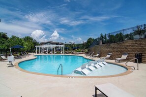 A swimming pool with lounge chairs and umbrellas, surrounded by a brick wall and trees. - Landing | Chic 1BD, Gym (Gainesville)