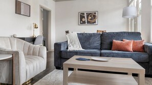 Ein Wohnzimmer mit grauem Sofa, einem weißen Sessel, einem Holztisch und einer Lampe.