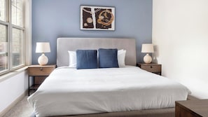 Une chambre d’hôtel avec un grand lit, deux tables de chevet, une fenêtre et une œuvre d’art murale.