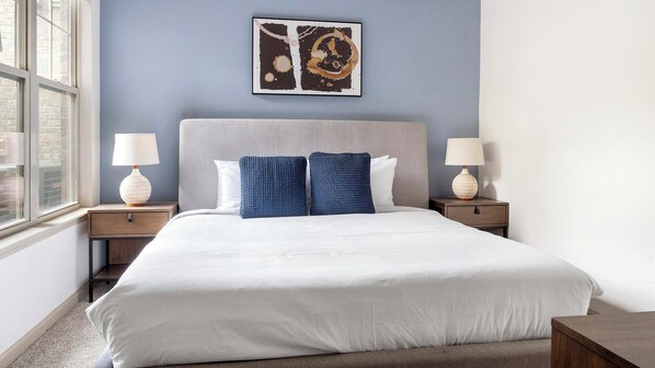 A hotel room with a large bed, two nightstands, a window, and a wall art piece.