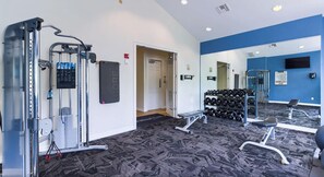 Ein Fitnessraum mit Trainingsgeräten, einem Spiegel und einem an der Wand befestigten Hantelständer.