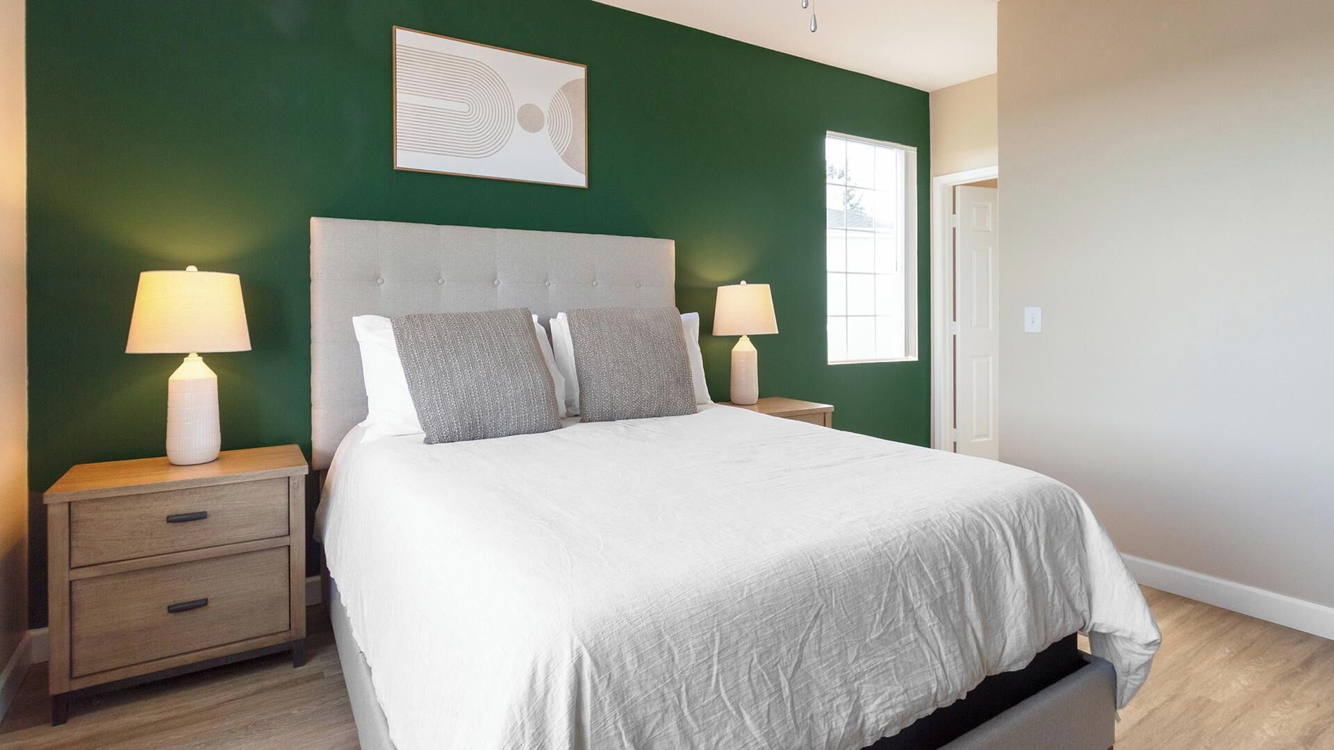 Une chambre à coucher avec un grand lit, deux tables de chevet, une commode, une œuvre d’art accrochée au mur et une fenêtre.