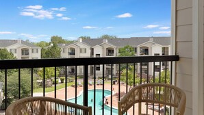 A residential area with a swimming pool, multiple houses, and a balcony with wicker chairs. - Landing | Modern 2BD, Yoga Studio, Pool (Lakewood)