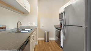 A compact kitchen with a stainless steel refrigerator, a built-in oven, and a sink. - Landing | Modern 2BD, Yoga Studio, Pool (Lakewood)