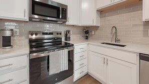 A modern kitchen with white cabinetry, stainless steel appliances, and a tiled backsplash. - Landing | Chic 1BD in Kannapolis (Kannapolis)