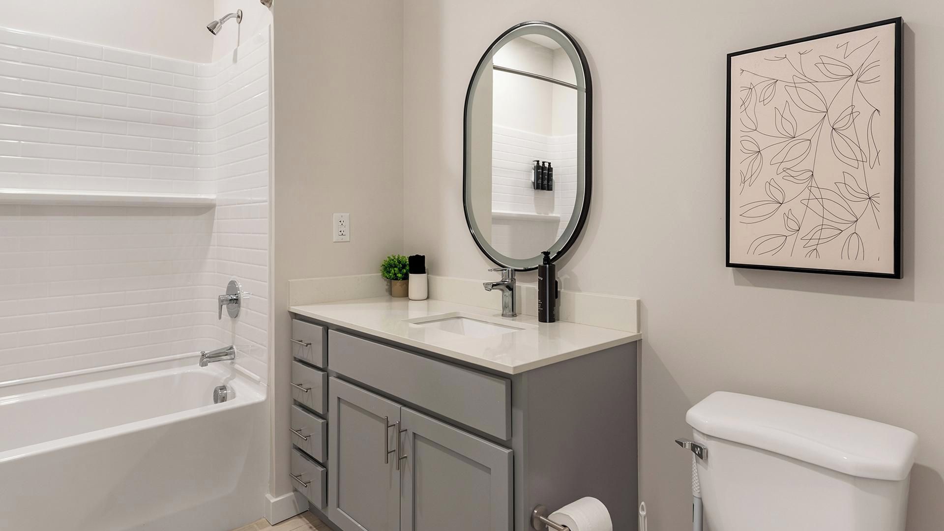 Een badkamer met een bad, een wastafel met spiegel, een toilet en een kunstwerk in een lijst aan de muur.