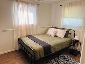 A single bed with a metal frame, a bedside table with a lamp, and a patterned rug on a wooden floor.