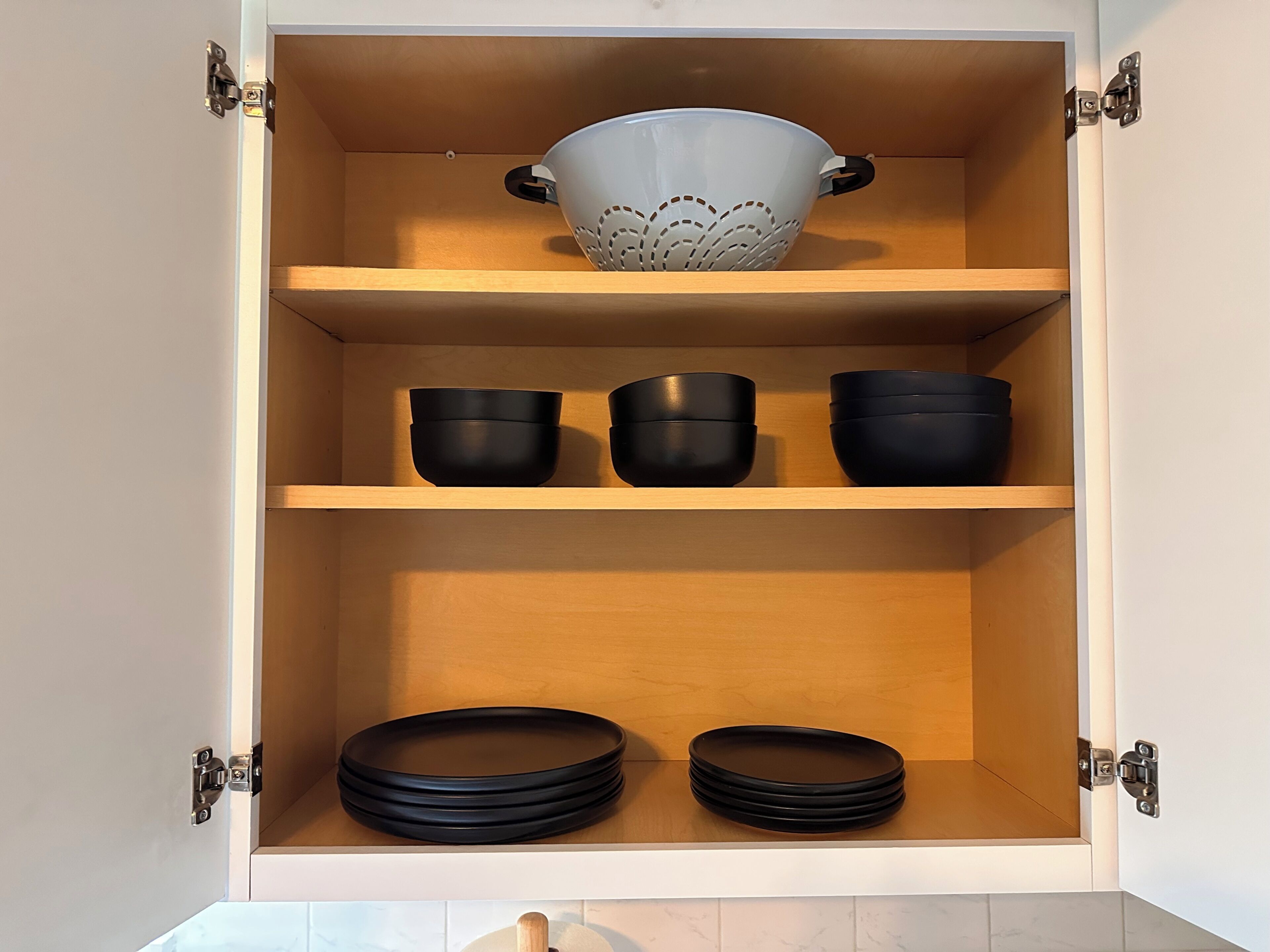 A kitchen cabinet with three shelves, each holding black bowls and plates.