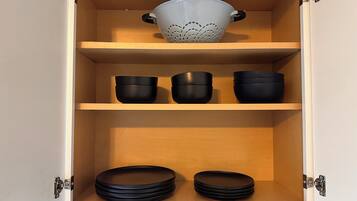 A kitchen cabinet with three shelves, each holding black bowls and plates.