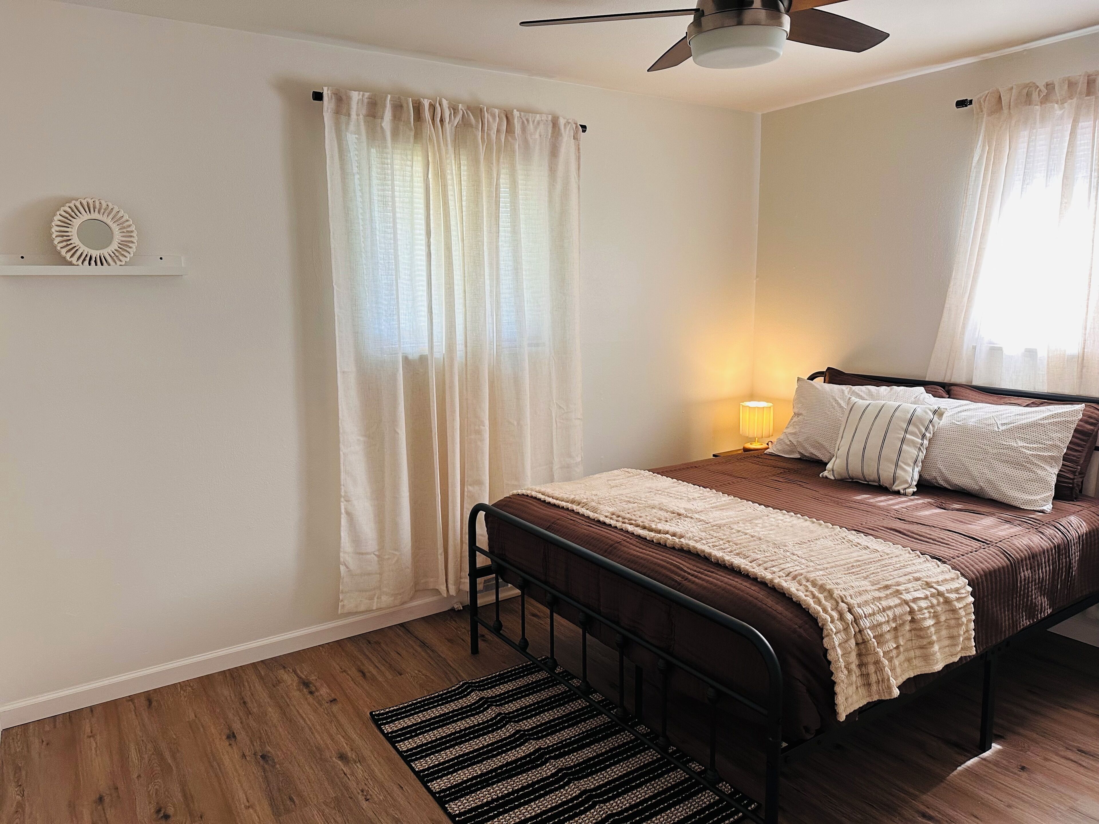 Une chambre à coucher avec un lit, une lampe de chevet, un ventilateur de plafond et une fenêtre avec des rideaux.