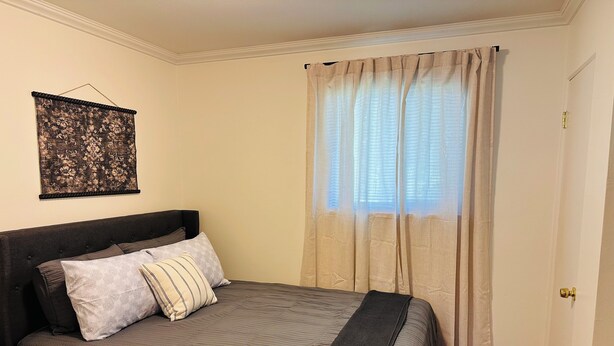 A bedroom with a bed, a headboard, a wall-mounted artwork, a window with curtains, and a door.