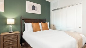 A neatly made bed with white and brown pillows, a bedside lamp, and a wooden nightstand with drawers. - Landing | Incredible Studio in Kannapolis (Kannapolis)