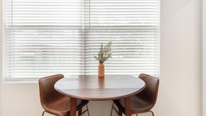 A round dining table with two chairs, a vase with a plant, and white blinds in the background. - Landing | Incredible Studio in Kannapolis (Kannapolis)