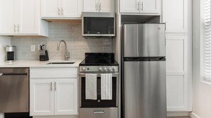 A modern kitchen with white cabinets, a stainless steel refrigerator, a built-in oven, and a coffee maker. - Landing | Incredible Studio in Kannapolis (Kannapolis)