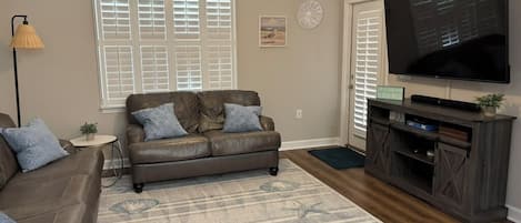 A living room with a leather sofa, a flat-screen TV, and a patterned rug.