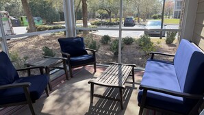 A sunlit patio with outdoor seating, including a bench and chairs, overlooking a parking area and a building. - 3-bedroom condo in beautiful Calabash golf course community (Calabash)