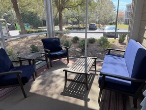 Eine sonnige Terrasse mit Sitzmöglichkeiten im Freien, darunter eine Bank und Stühle, mit Blick auf einen Parkplatz und ein Gebäude.