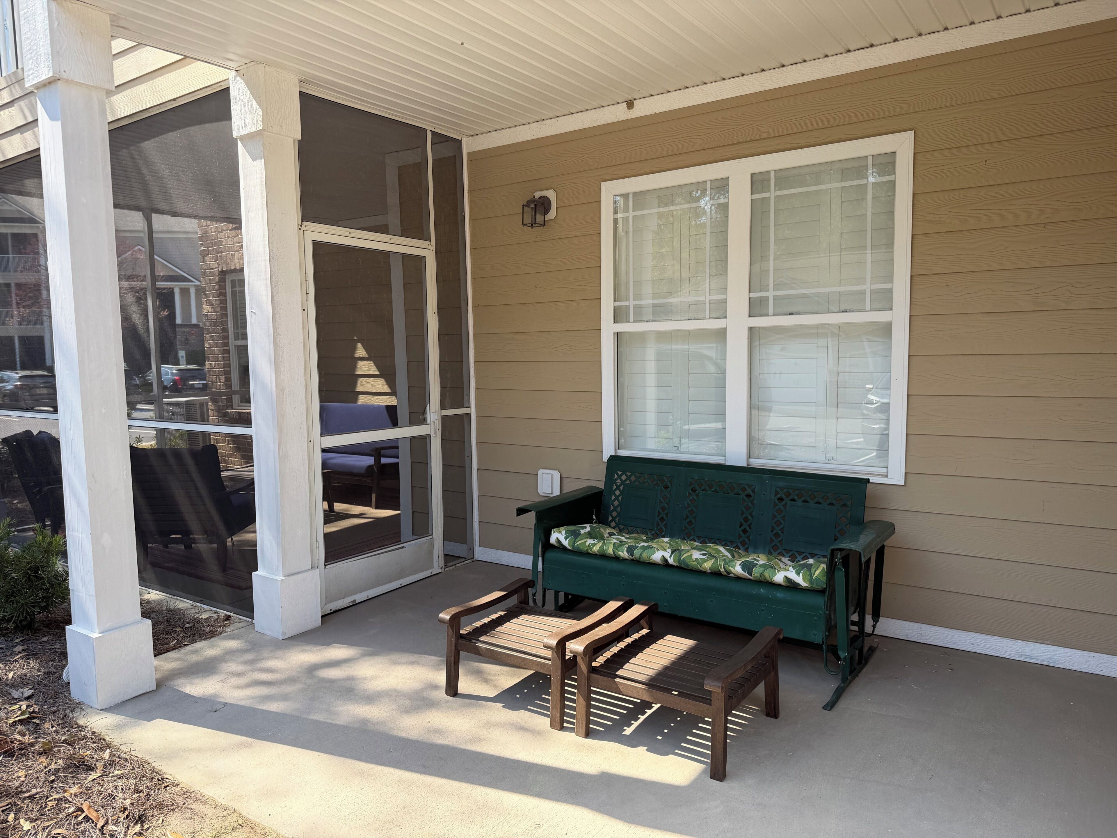 A covered porch with a bench and chairs, a window, and a door leading to a covered area.