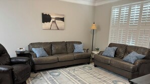 A living room with a brown leather sofa, a patterned rug, a lamp, and a window with blinds. - 3-bedroom condo in beautiful Calabash golf course community (Calabash)