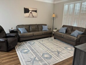 A living room with a brown leather sofa, a patterned rug, a lamp, and a window with blinds.