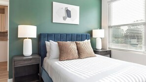 A bedroom with a bed, two bedside tables, a headboard, and a window with blinds. - Landing | Incredible 1BD in Kannapolis (Kannapolis)