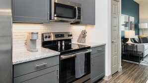 A modern kitchen with grey cabinetry, a built-in microwave, a stove, and a coffee maker. - Landing | Incredible 1BD in Kannapolis (Kannapolis)