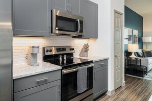 A modern kitchen with grey cabinetry, a built-in microwave, a stove, and a coffee maker. - Landing | Incredible 1BD in Kannapolis (Kannapolis)
