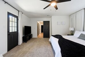Ein Hotelzimmer mit einem Bett, einem Fernseher, einem Deckenventilator und einer Tür zu einem anderen Raum.