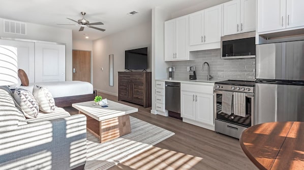 Une chambre d’hôtel moderne équipée d’un lit, d’un coin salon, d’une kitchenette avec une cuisinière et un four à micro-ondes, et d’un ventilateur de plafond.