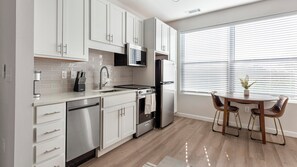 A modern kitchen with white cabinets, stainless steel appliances, and a dining area with a wooden table and chairs. - Landing | Stylish Studio in Kannapolis (Kannapolis)