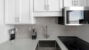 Une cuisine moderne avec des meubles blancs, une hotte en acier inoxydable, un four à micro-ondes encastré, une bouilloire et un évier.