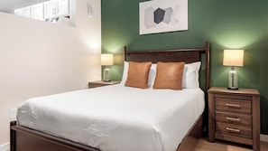 A neatly made bed with white linens, two brown pillows, and a wooden headboard. There are two bedside tables with lamps, one on each side of the bed. - Landing | Modern 1BD in Kannapolis (Kannapolis)