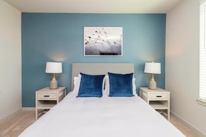 A bedroom with a bed, two bedside tables, two lamps, a headboard, and a wall-mounted picture.