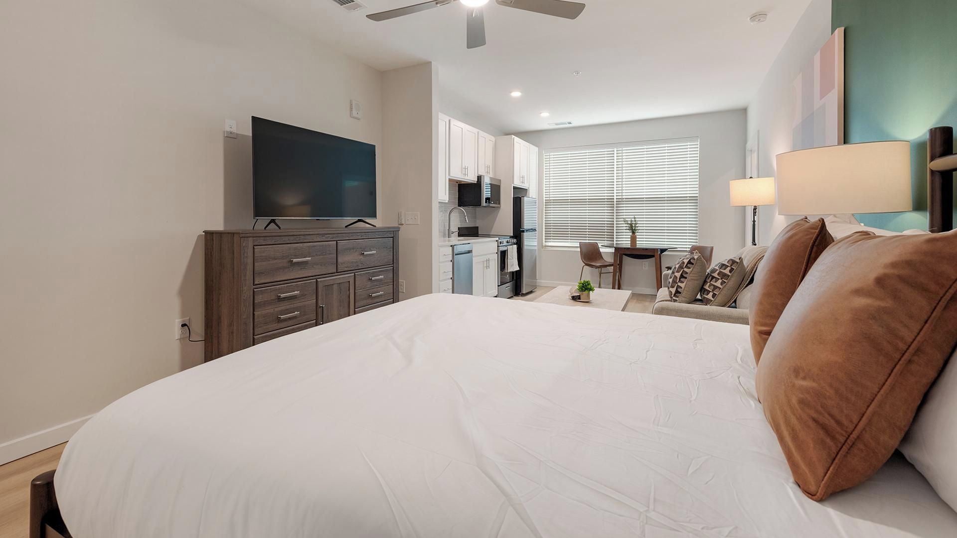 Een moderne hotelkamer met een groot bed, een flatscreen-tv, een kitchenette en een raam met zonwering.