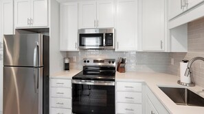 A modern kitchen with stainless steel appliances, white cabinetry, and a tiled backsplash. - Landing | Modern 1BD in Kannapolis (Kannapolis)