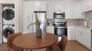A modern kitchen with white cabinetry, stainless steel appliances, and a round wooden dining table with chairs. - Landing | Modern 1BD in Kannapolis (Kannapolis)
