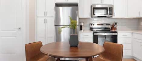 A modern kitchen with white cabinets, stainless steel appliances, and a round wooden table with two chairs.