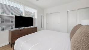 A bedroom with a large bed, a TV on a wooden dresser, white walls, and two white doors. - Landing | Modern 1BD in Kannapolis (Kannapolis)