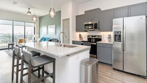 A modern kitchen with a central island, stainless steel appliances, and a large window offering a city view. - Landing | Modern 1BD in Kannapolis (Kannapolis)