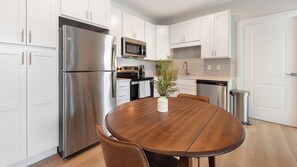 A modern kitchen with white cabinetry, stainless steel appliances, and a round wooden dining table. - Landing | Modern 1BD in Kannapolis (Kannapolis)
