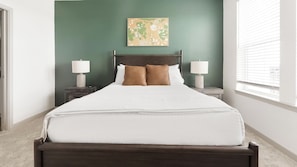 A neatly made bed with white bedding, two bedside tables with lamps, a green wall, and a window with blinds. - Landing | Stylish 1BD, Gym, Pool (Port Charlotte)