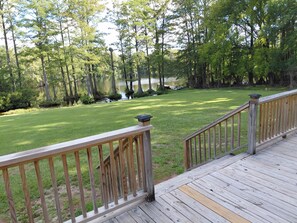 A wooden deck with a railing overlooking a grassy area and a body of water.